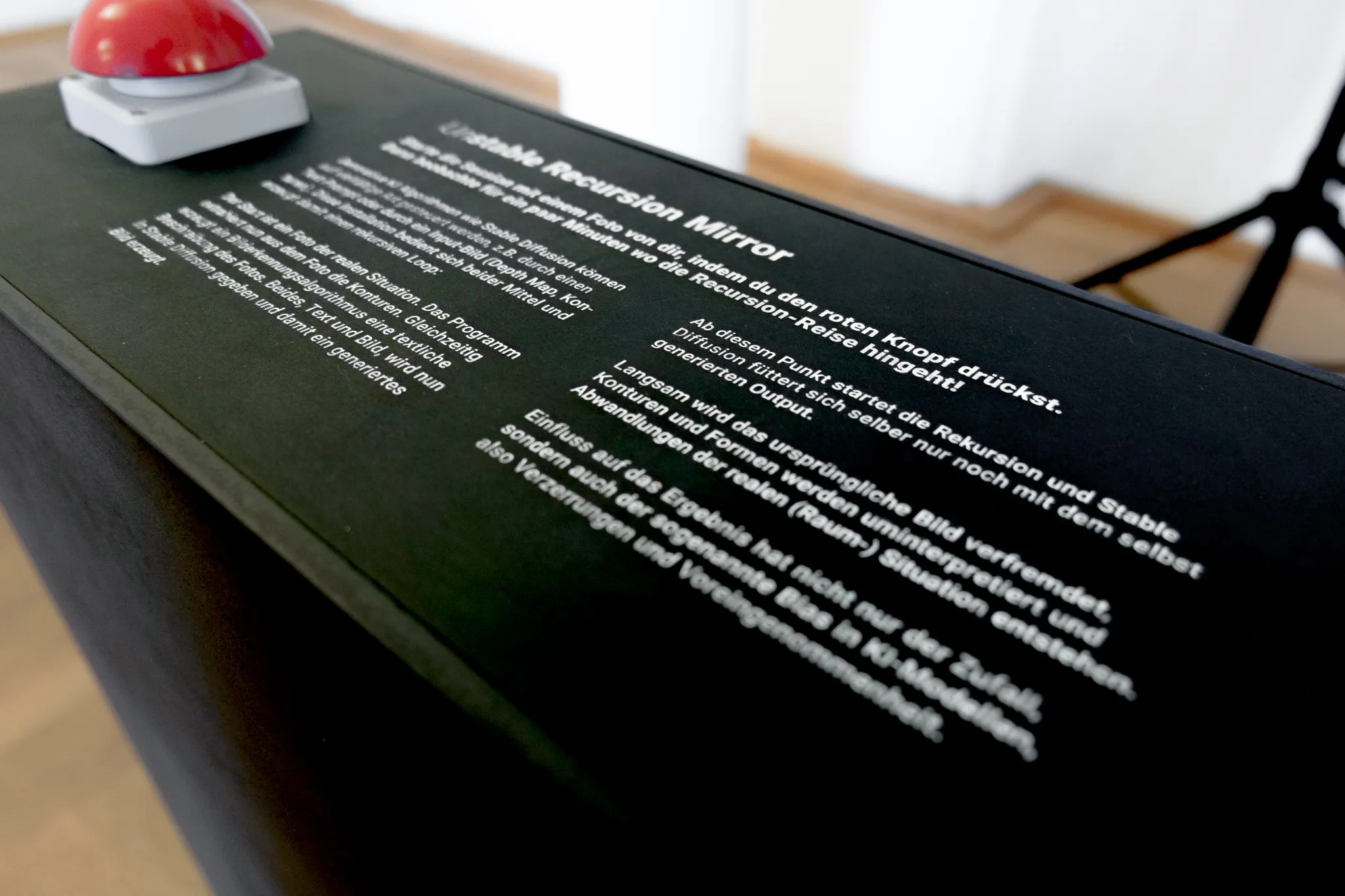 Close-up of the black plinth: the red buzzer beside white printed German instructions headed “Unstable Recursion Mirror”, inviting visitors to press the red button and watch the recursion journey for a few minutes