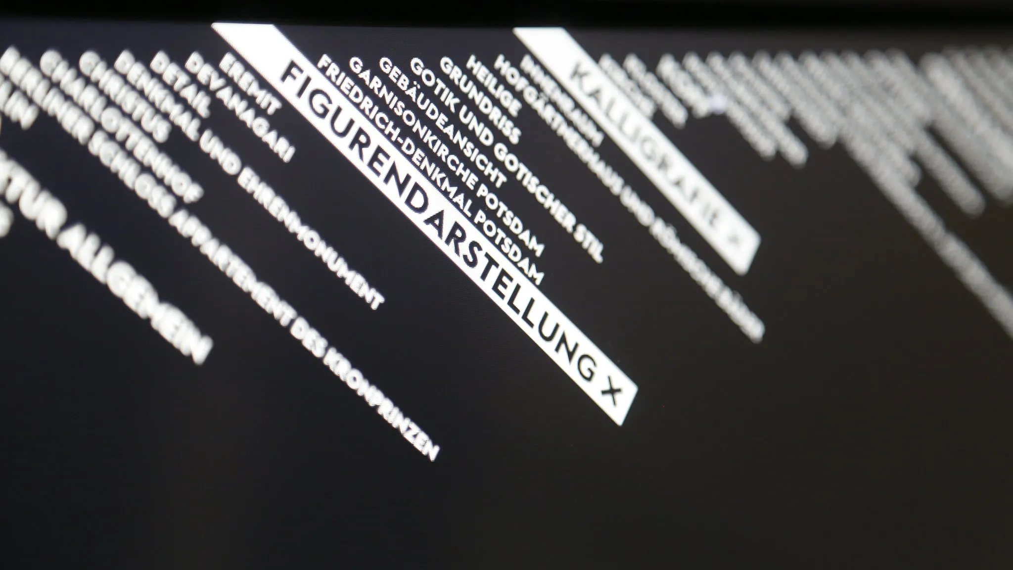Close-up of the diagonal keyword labels on the screen, with »Figurendarstellung« and »Kalligrafie« highlighted as active filters and the other keywords blurring out of focus