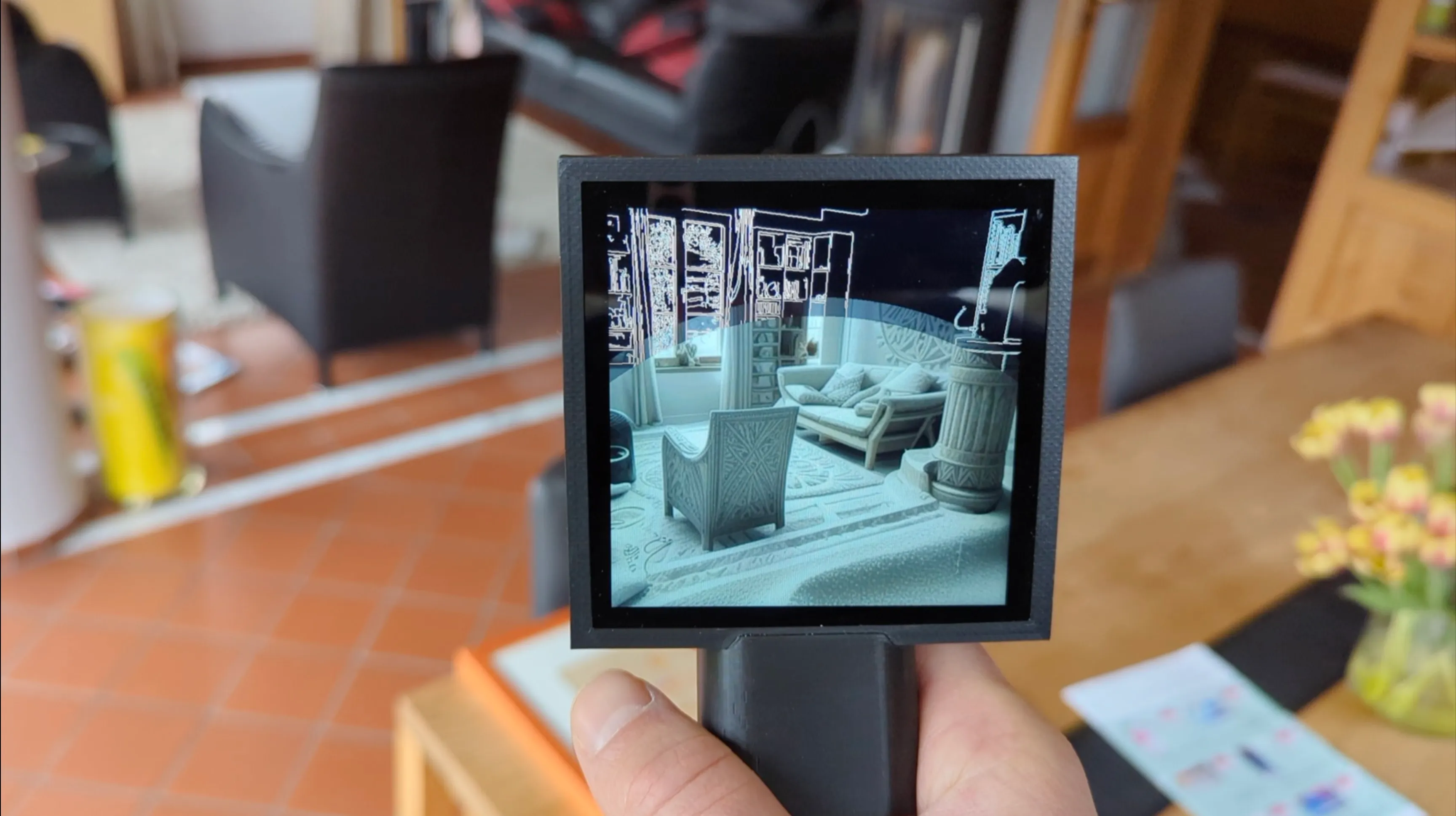 A hand holds Transferscope up in a living room; its screen shows the room re-rendered in the texture of sand sampled just before, with white edge lines still tracing the shelves along the top.