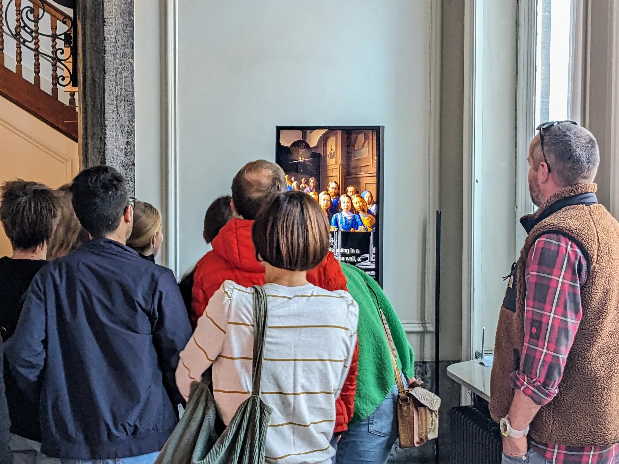 A crowd of visitors gathers in a tall, white-paneled room in front of unStable Mirror, whose screen shows them re-rendered as a Renaissance-style group portrait