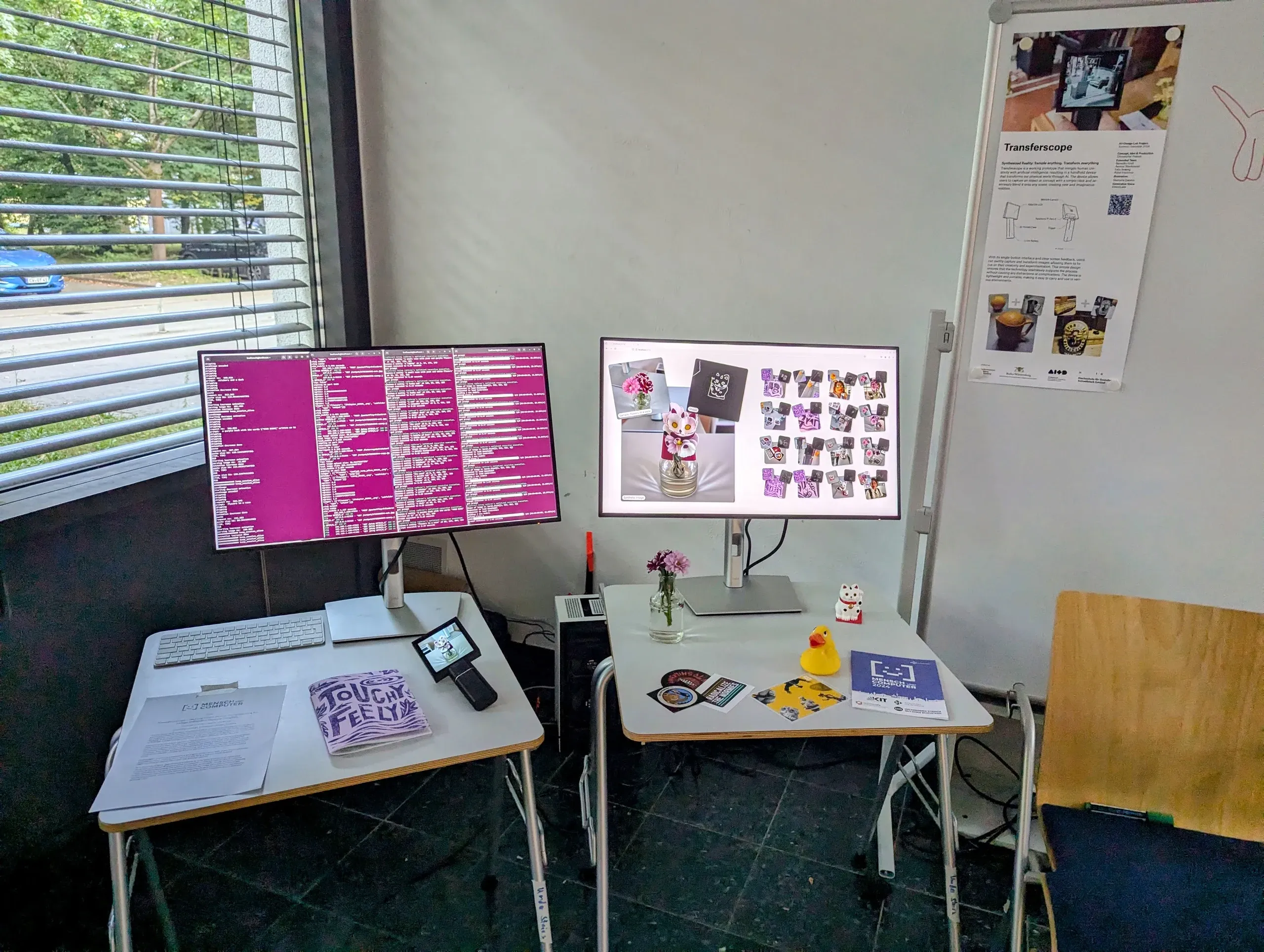 Demo corner with two monitors on small tables, one full of magenta terminal logs, the other showing a vase of flowers remade as a lucky-cat figure beside a grid of earlier results, with Transferscope lying on the left table and a Transferscope poster on a stand behind.