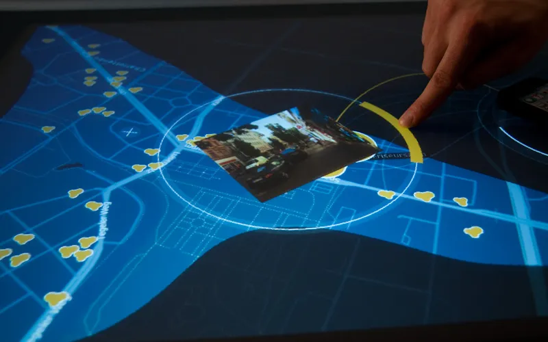 A photo left at a place opens inside a circular frame on the map while a finger drags the yellow arc of the radial selector; yellow place markers line the blue streets around it