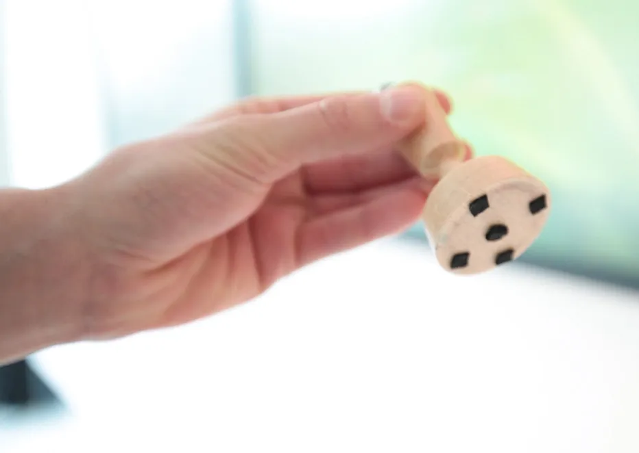 The finished wooden stamp held upside down, five black conductive pads on its round base