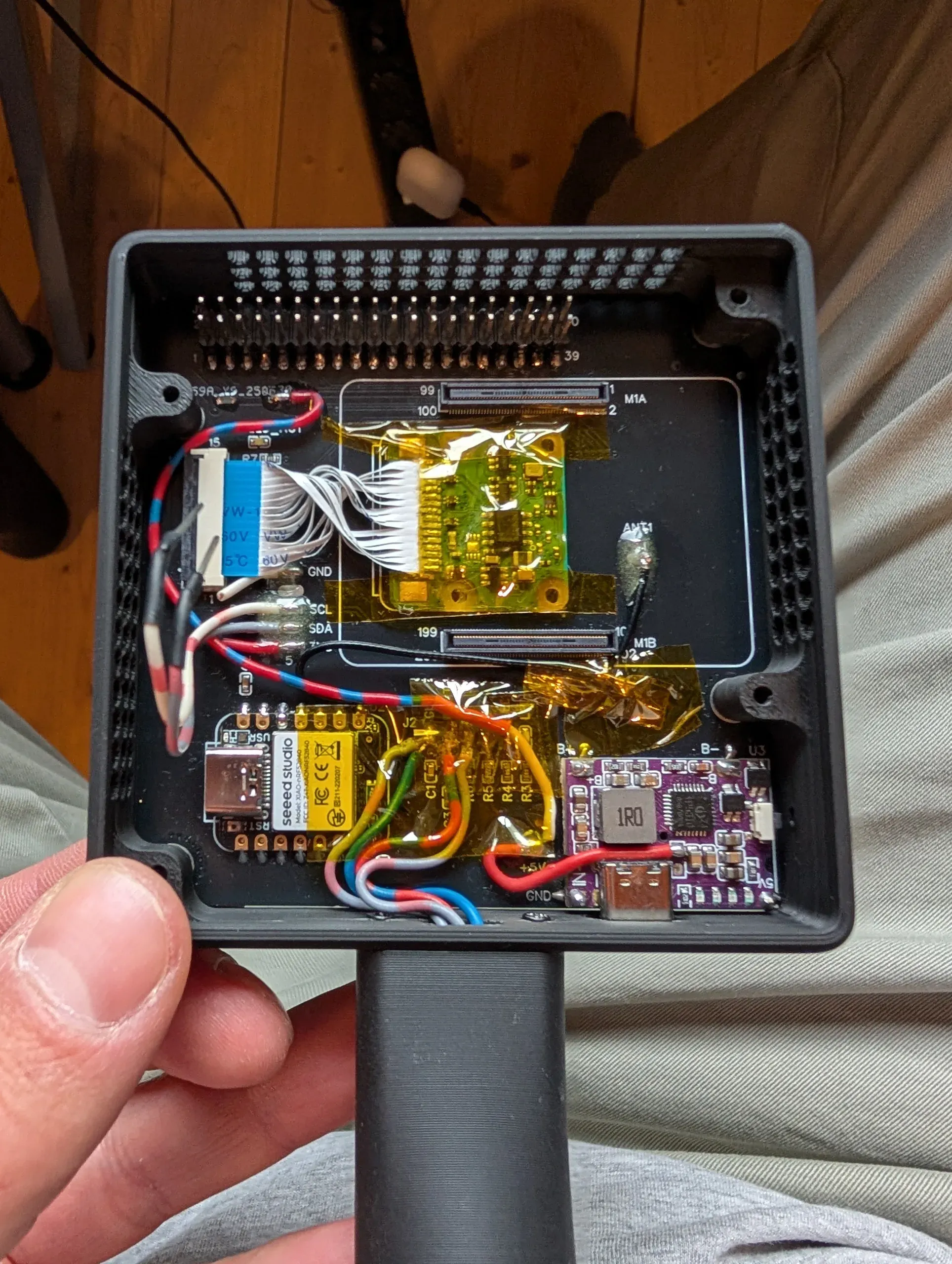 Close-up of the first board revision inside the opened body, with its header pins, the taped ribbon-cable adapter, a Seeed Studio XIAO microcontroller and the purple charging board
